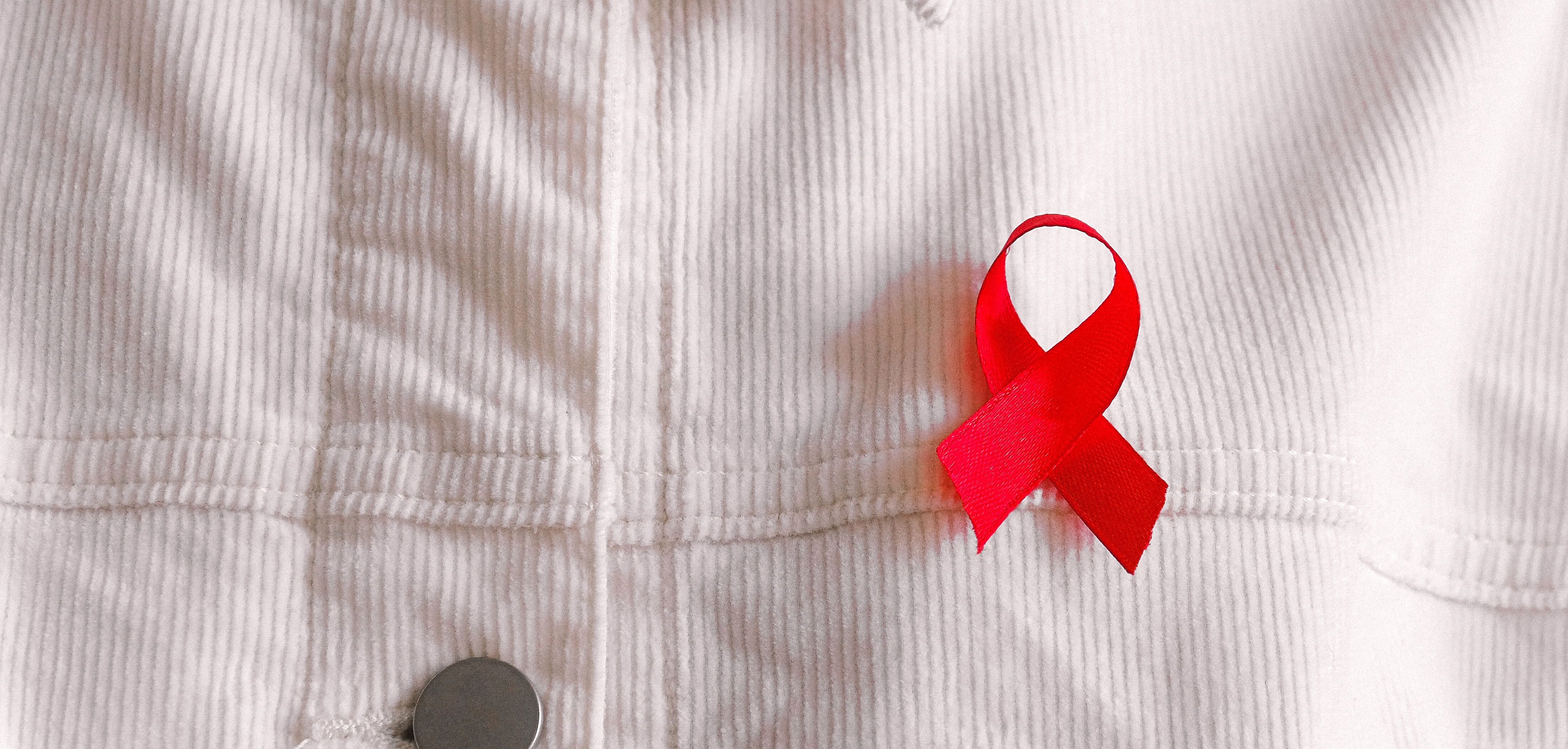 photo of man wearing white button down shirt with red AIDS ribbon